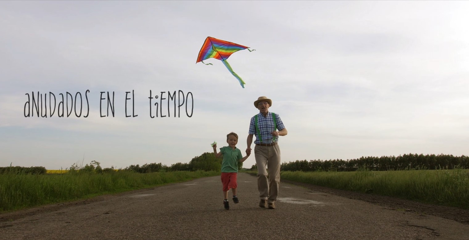 Fotograma final del documental, persona mayor y niño corriendo tras una cometa y el texto "Anudados en el tiempo"