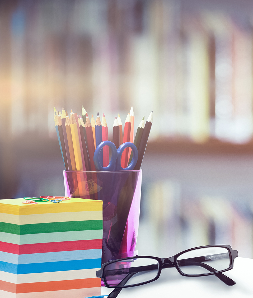 Foto de un escritorio con un lapicero, libros y unas gafas y al fondo una estantería