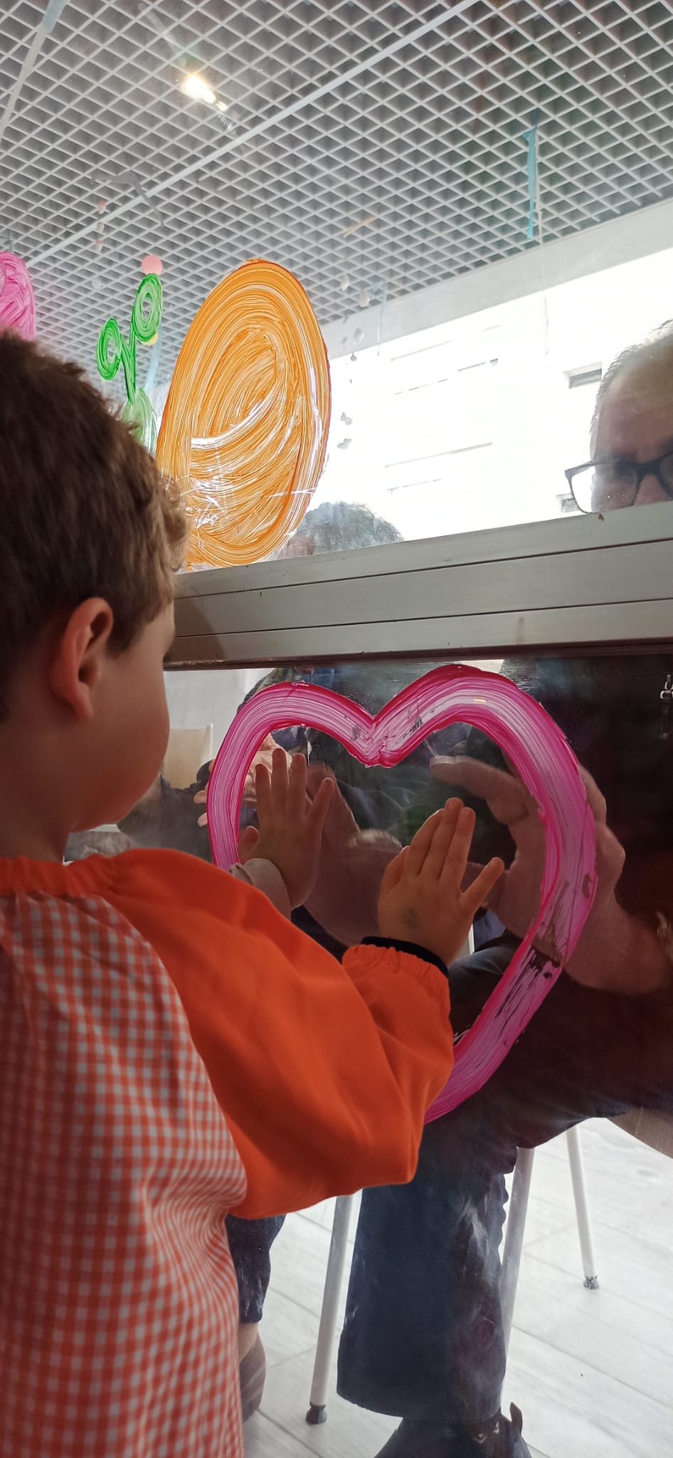Un niño pequeño une sus manos con las de una persona mayor a través de un corazón pintado en una cristalera