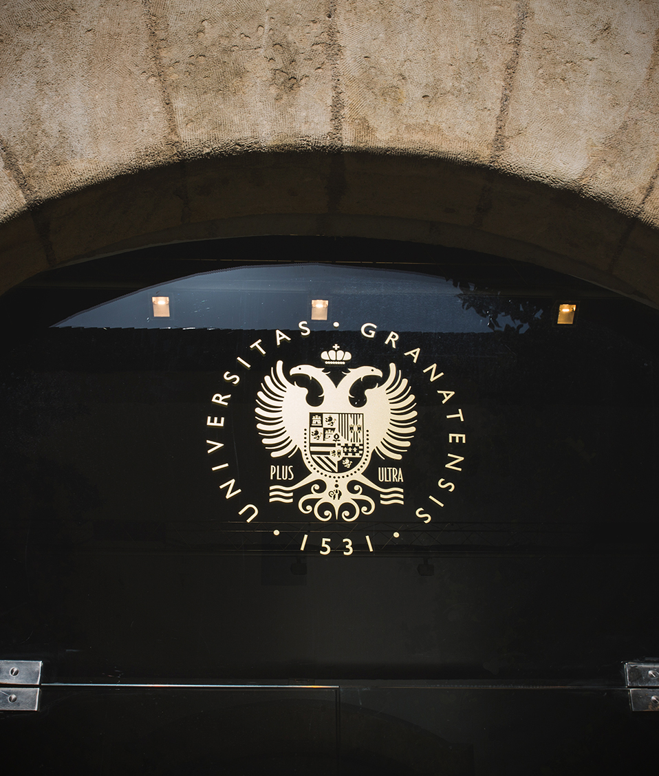 Detalle puerta de cristal en Patio del Hospital Real con escudo UGR en vinilo dorado en la parte superior